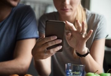 Close up of woman holding mobile phone, with her partner cropped on the left.