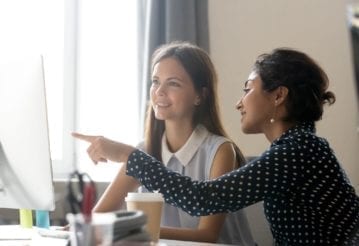 Happy intern listening to their mentor explaining a computer task