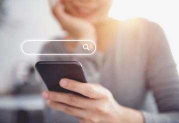 Closeup of a woman using a mobile phone with a search input field graphic above the phone