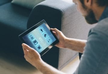 A man interacts with a touchscreen tablet at home.