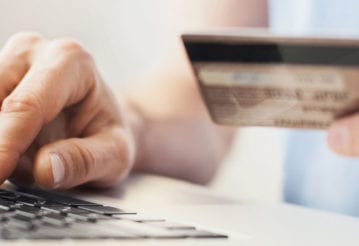 A hand holds a credit card, while the other types on a laptop keyboard