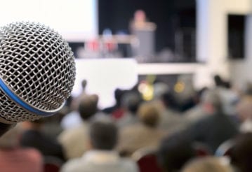 Close up of a microphone with a stage and audience out of focus in the background