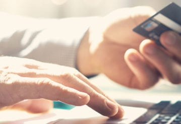 A hand holds a credit card, while the other types on a laptop keyboard