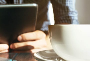 Man holding a computer tablet. There is a coffee mug in the foreground.