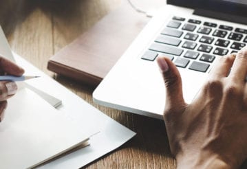 Close up of hands. One is typing, the other holds a pencil.