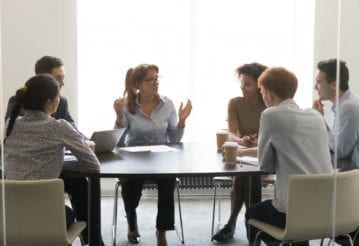 Female executive talking to coworkers at a corporate briefing, sitting at a conference table in a boardroom