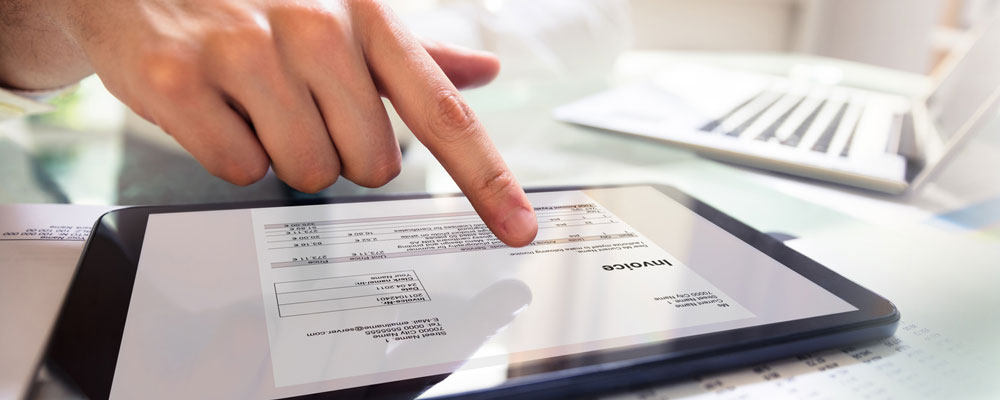 Close-up Of A Businessperson's Hand Analyzing Bill On Digital Tablet Over Desk