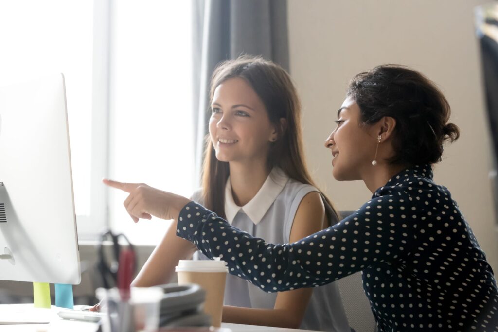 Happy intern listening to their mentor explaining a computer task