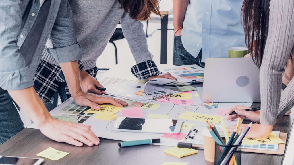 Close up of an office table covered in brainstorming notes. Several people are leaning over the notes.