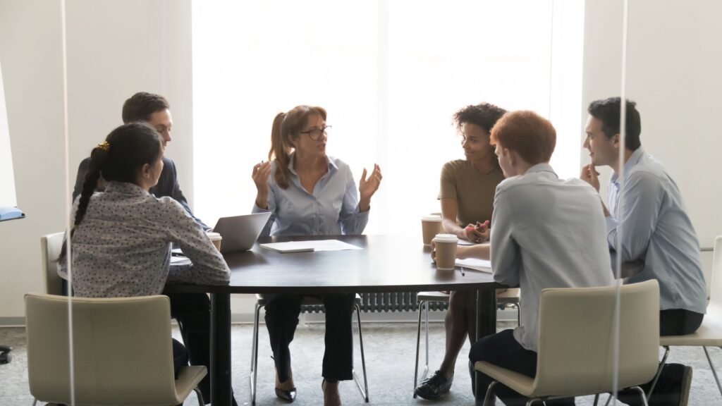 Female executive talking to coworkers at a corporate briefing, sitting at a conference table in a boardroom