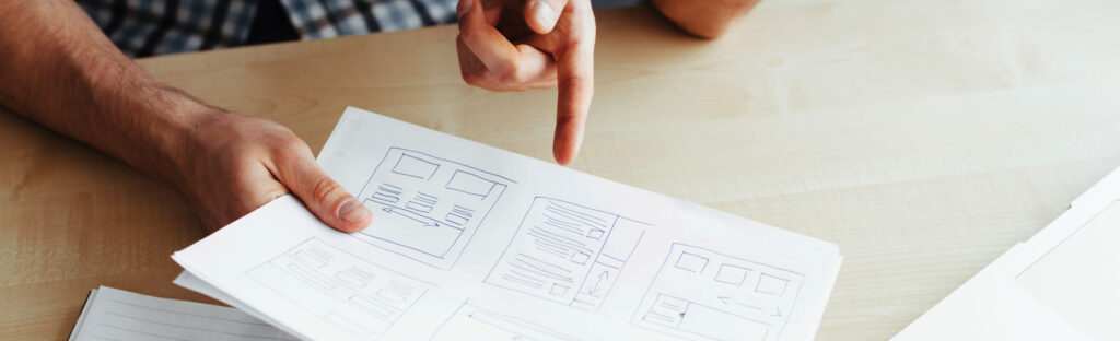 A man's hands hold drawn mock ups of a website design