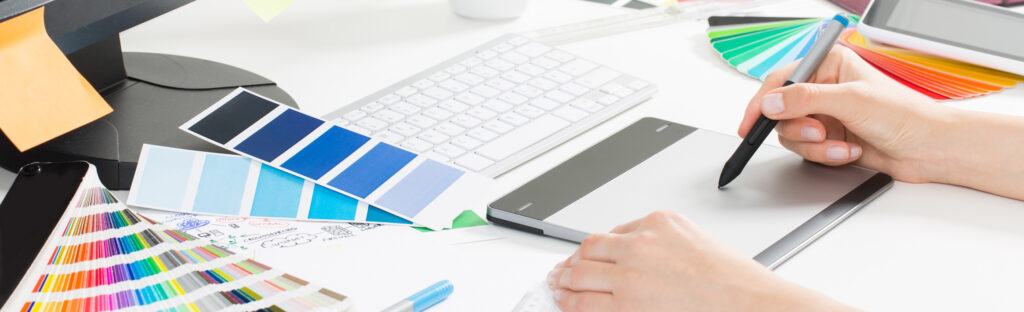 A designer using a drawing tablet with colour swatches on their desk.