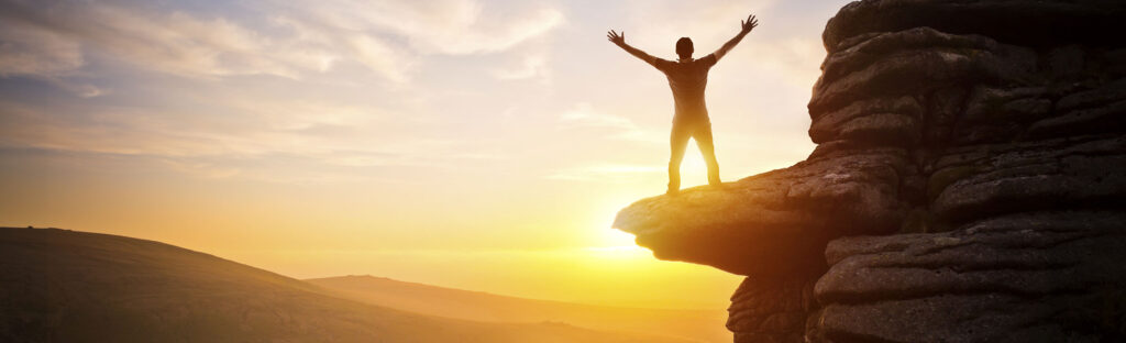 Man with his arms up, stand on a cliff