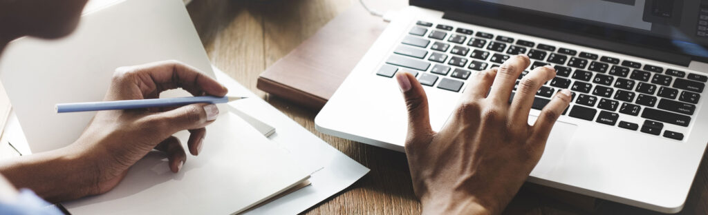 Close up of hands. One is typing, the other holds a pencil.