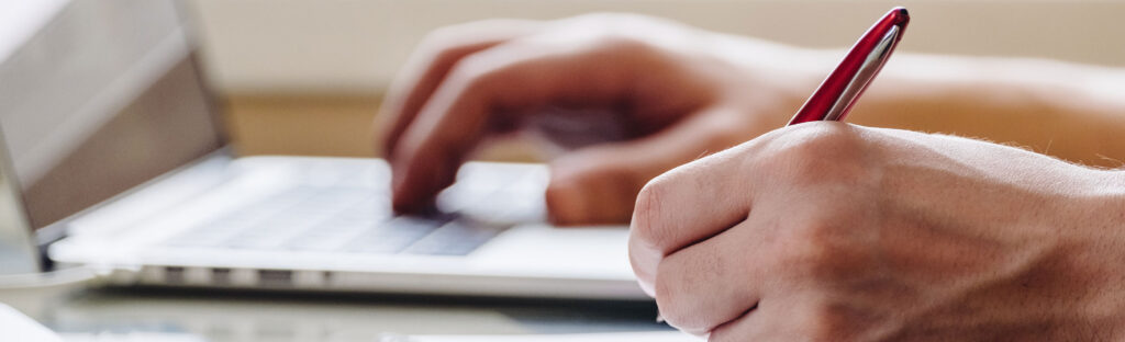 Close up of hands. One is typing, the other holds a pen.