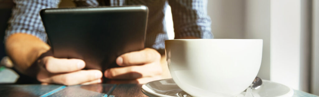 Man holding a computer tablet. There is a coffee mug in the foreground.