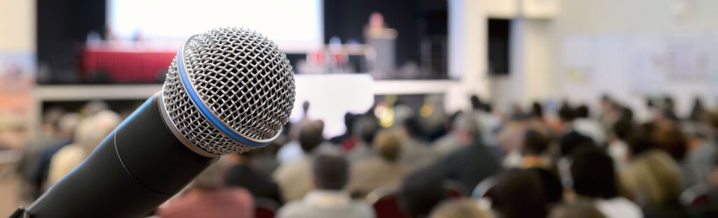 Close up of a microphone with a stage and audience out of focus in the background
