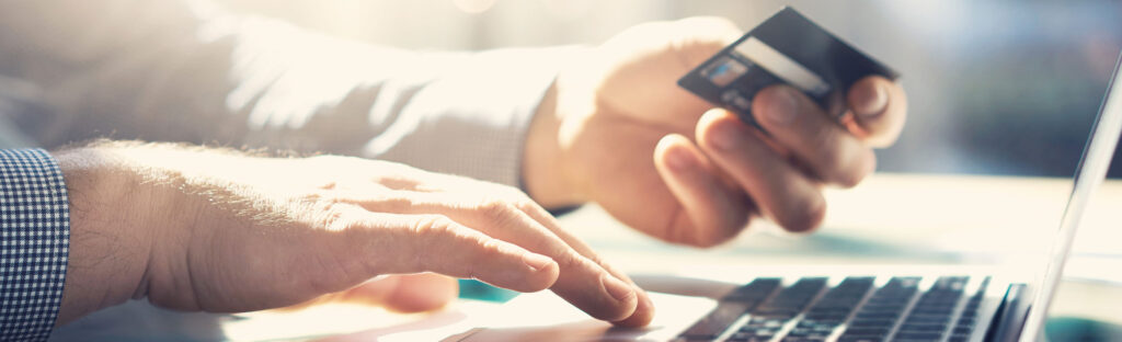 A hand holds a credit card, while the other types on a laptop keyboard