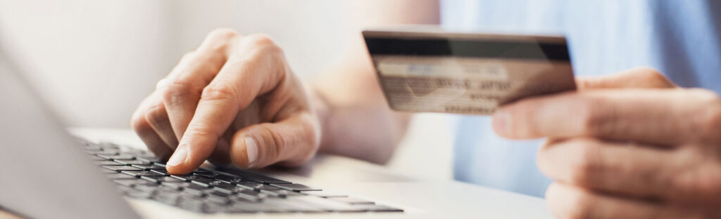 A hand holds a credit card, while the other types on a laptop keyboard