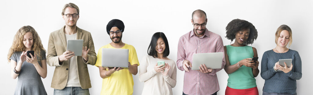 Smiling young adults standing in a line looking at their electronic devices.