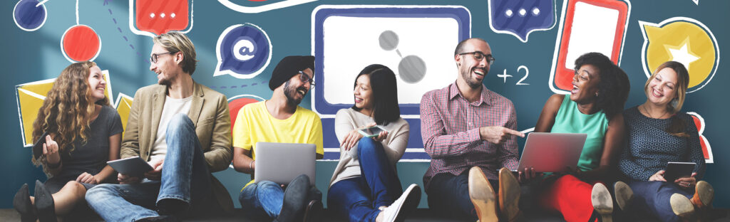 Group of people sitting on the floor in front of a decorated wall. They each hold electronic devices such as phones, laptops, or tablets.