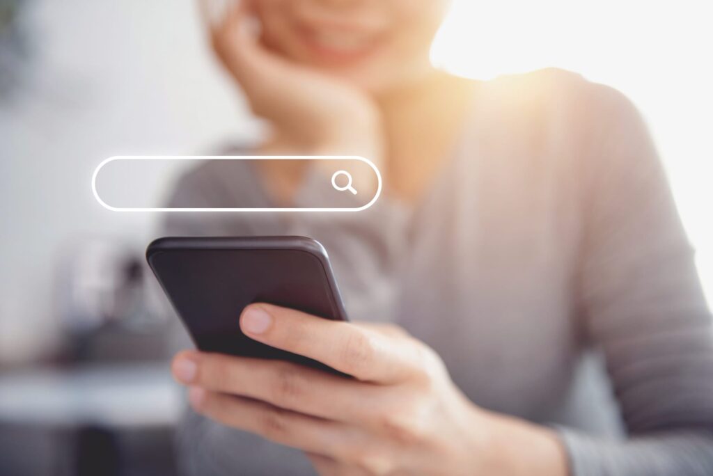 Closeup of a woman using a mobile phone with a search input field graphic above the phone