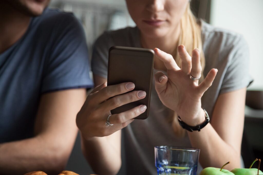 Close up of woman holding mobile phone, with her partner cropped on the left.